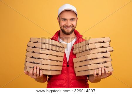 Horizontal Shot Of Happy Man Holds Two Piles Of Carton Boxes With Pizza, Has Surprised Joyful Expres