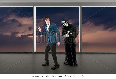 Man In A Halloween Grim Reaper Ghost Costume Chasing, Mocking And Making Fun Of Scared Businessman R