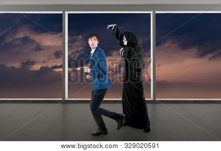 Man In A Halloween Grim Reaper Ghost Costume Chasing, Mocking And Making Fun Of Scared Businessman R