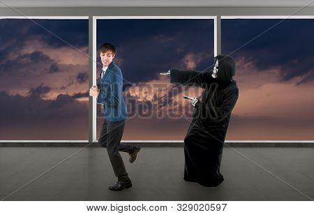 Man In A Halloween Grim Reaper Ghost Costume Chasing, Mocking And Making Fun Of Scared Businessman R