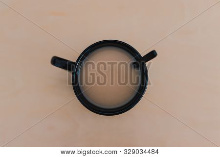 hot bevereages, chai tea with milk in black mug on wooden table of the same color shot from above to