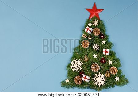 Christmas tree made of natural spruce branches deecor with red star on blue background, flat lay card with copy space