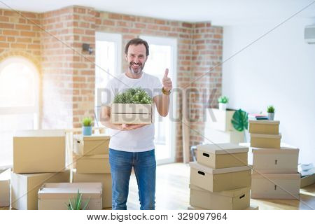 Middle age senior man moving to a new house packing cardboard boxes happy with big smile doing ok sign, thumb up with fingers, excellent sign