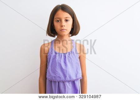 Young beautiful child girl wearing purple casual dress standing over isolated white background with serious expression on face. Simple and natural looking at the camera.