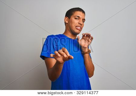 Young handsome arab man wearing blue t-shirt standing over isolated white background disgusted expression, displeased and fearful doing disgust face because aversion reaction. With hands raised