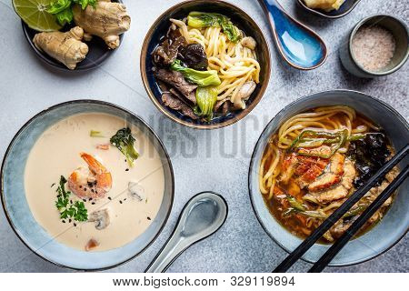 Set Of Serving Asian Soups On Gray Background Top View. Tom Yum Soup, Eel Fish Soup And Ramen Noodle