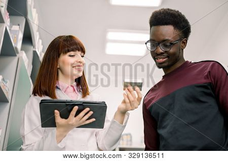 Young Smiling Caucasian Woamn Pharmacist Holding Digital Tablet Explaining Prescribed Medicine To Yo