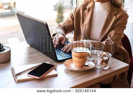 Beautiful Business Woman Sitting In Cafe Andworking. There Are Laptop, Smartphone And Cup Of Coffee.