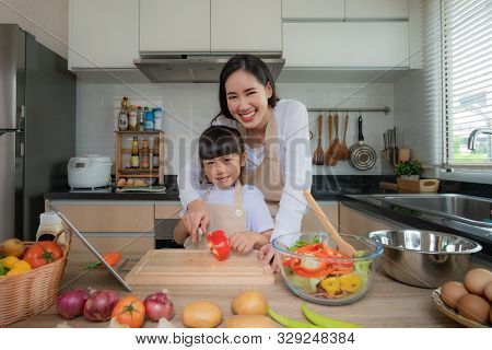 Portrait Of Beautiful Asian Young Woman And Her Daughter Cooking Salad For Lunch Using Online Intern