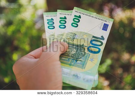 Male Hand Holding 100 Hundredth Euro Banknotes On Green Background Outdoors, Closeup