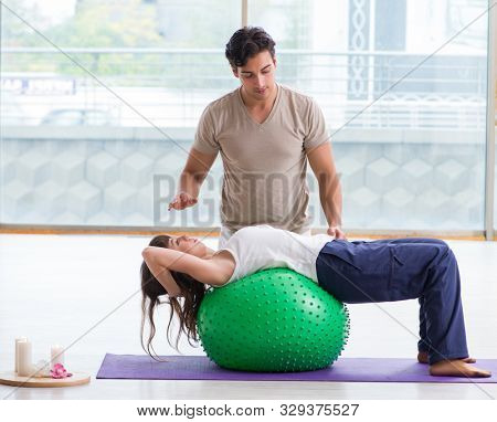 Personal coach helping woman in gym with stability ball