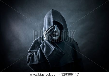 Ghostly figure in hooded cloak. Scary figure with part of mannequin head in hands 