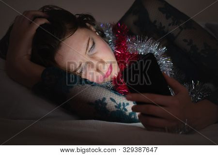 Texting, Using A Phone After A Party In Bed. Young Woman In A Party Dress With A Smartphone In Bed A