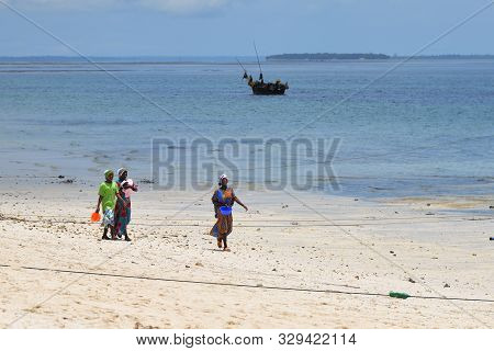 Kendwa, Zanzibar - October 4, 2019: Local Women In Traditional Dress Going Along The Ocean Shore Dur