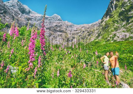 New Zealand trampers tourists taking selfie photo with camera phone in lupins flowers mountains background on summer road trip. Happy camping couple walking in nature taking pictures in New Zealand.