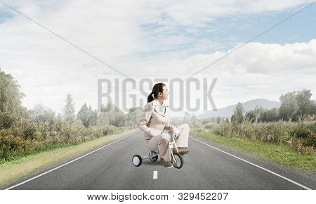 Caucasian Woman Riding Kids Bicycle On Asphalt Road. Young Employee In White Business Suit Biking Ou
