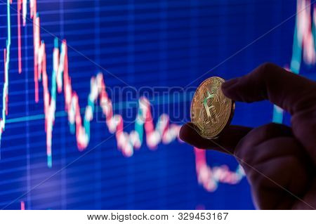 Hand Holding Bitcoin Shiner On Blurry Dark Blue Exchange Chart