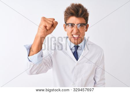 Young handsome sciencist man wearing glasses and coat over isolated white background angry and mad raising fist frustrated and furious while shouting with anger. Rage and aggressive concept.