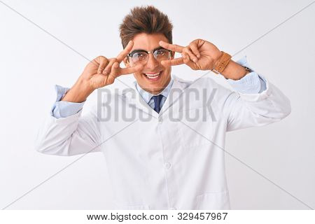 Young handsome sciencist man wearing glasses and coat over isolated white background Doing peace symbol with fingers over face, smiling cheerful showing victory