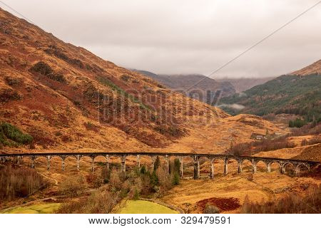 Glenfinnan Viaduct In-between Wintery Brown Fields And Hills On A Cloudy Day In The Scottish Highlan