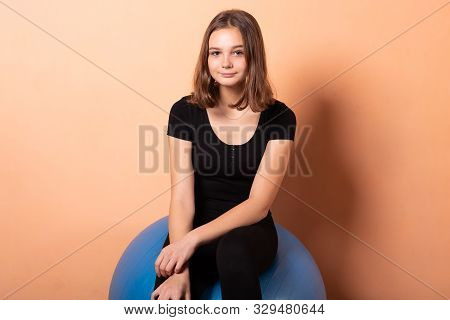 Girl On A Gym Ball, On A Light Orange Background.