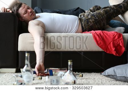 Portrait Of Lying Man Drunkard Lying On Comfortable Sofa And Holding Bottle Of Expensive Alcohol. Be