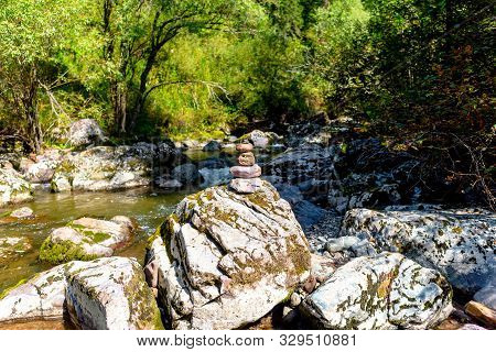 A Pyramid Of Flat Round Stones Stands On A Large Stone In The Middle Of A Mountain Rapid River In Th