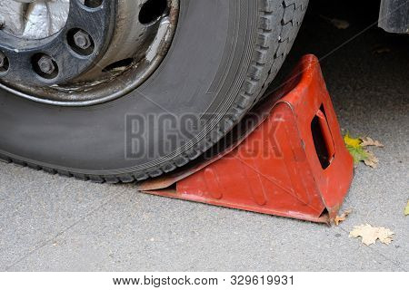 Red Wheel Chock Under The Wheel Of A Car Close-up. Car Repair. Metal Rack For Machine Repair.