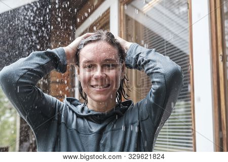 Happy Woman Enjoying The Warm Rain, Smiling Broadly And Looking At The Camera, Against A Background 