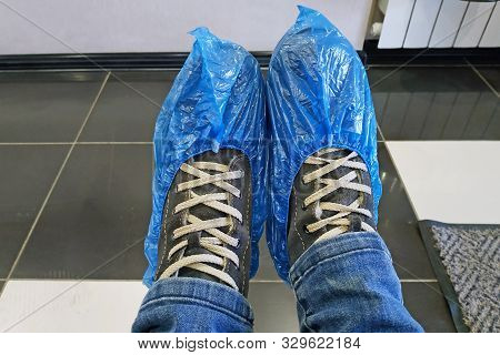 Legs Shod In Boots And Blue Shoe Covers. Shoe Covers On The Legs Close-up. Legs In Shoe Covers Again