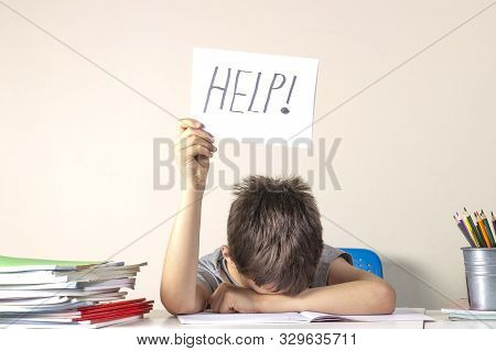 Sad Tired Frustrated Boy Sitting At The Table With Many Books And Holding Paper With Word Help. Lear