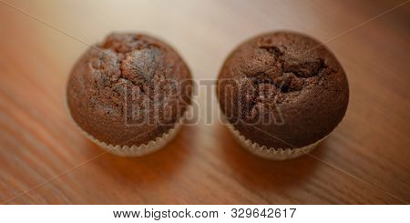 Two Chocolate Muffins On The Brown Wooden Table.