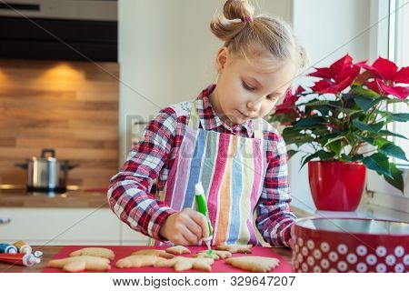 Pretty Little Girl With Funny Pigtails Decoraiting Christmas Cookies Of Different Forms In Kitchen