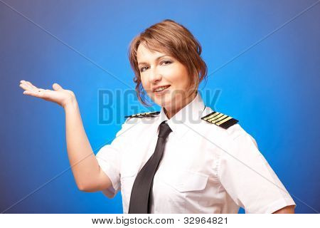Pilota donna bella indossa l'uniforme con spalline, presentando qualcosa sulla sua mano, in piedi