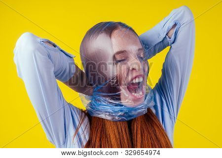 Redhaired Ginger European Woman Suffocation Head In Blue Polyethylene Package In Studio Yellow Backg