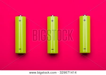 Top view of 3 yellow green AA alkaline or rechargeable NiMH batteries on pink background