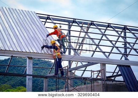 Roofer Worker In Protective Uniform Wear And Gloves, Using Air Or Pneumatic Nail Gun And Installing 