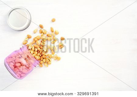 Roasted Organic Unsalted Peanuts Spilling From Pink Jar On Rustic White Wood Background. Shot From O