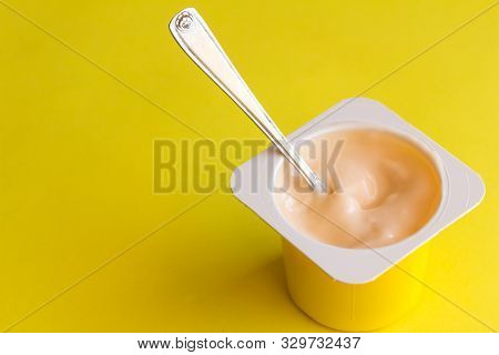 Yogurt In Plastic Pot With Small Spoon Isolated On Yellow Background