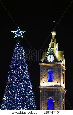 Blue Christmas Tree With A Blue Star Next To The Chapel And The Clock On The Tower On The Background