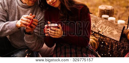 Romantic Couple In Love With Red Cups Of Hot Bevrage In The Picnic. Love Sign