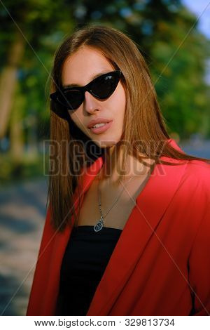 Blonde Girl In A Red Lady-type Pantsuit And Black Top, Watch, Ring, Pendant And Sunglasses Is Walkin
