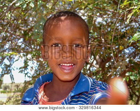 African kid with a blue t-shirt in the yard of the village in Botswana, against a bush background
