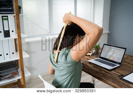 Young Woman Using Back Scratcher At Office