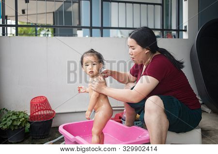 Asian Woman Washing Her Daughter In Bathtub, Baby Girl Taking A Bath In Pink Tub