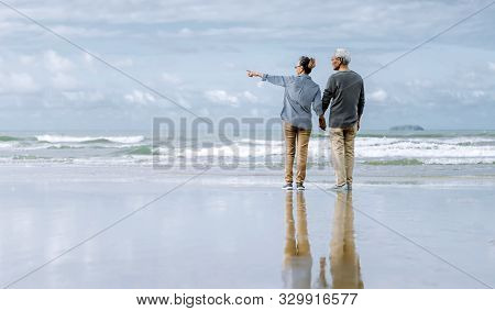 Asian Senior Couple Or Elderly People Walking And Siting At The Beach On Their Weekend Vacation Holi