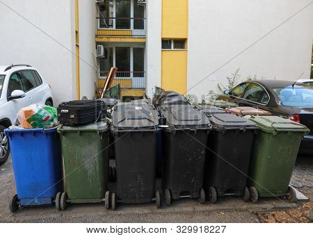 Shallow Depth Of Field Image With Plastic Garbage Bins Filled With Household Waste Near A Block Of F
