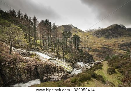 Beautiful Landscape Image Of Ogwen Valley River And Waterfalls During Winter With Snowcapped Mountai
