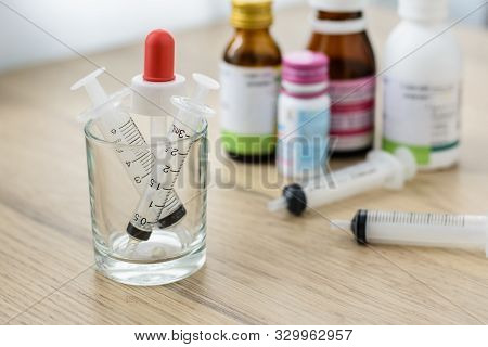 Empty Syringes Barrel In The Small Glass On The Wooden Table With Blured Medicine Bottle Background.