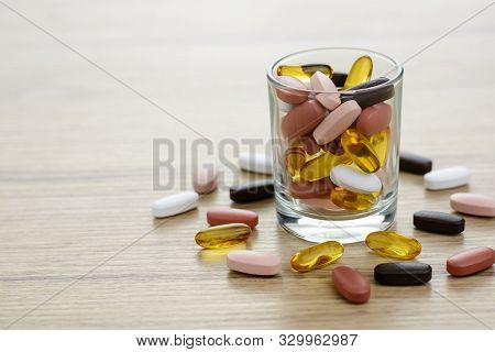 Fishoil Capsules And Multivitamin Supplements In The Small Glass On The Wooden Table With Copy Space